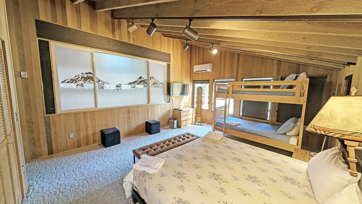 A welcoming family bedroom with a king-sized bed and a set of bunk beds, accented by warm wooden beams and mountain-themed artwork. A TV sits opposite the beds, making the space ideal for both relaxation and family bonding.