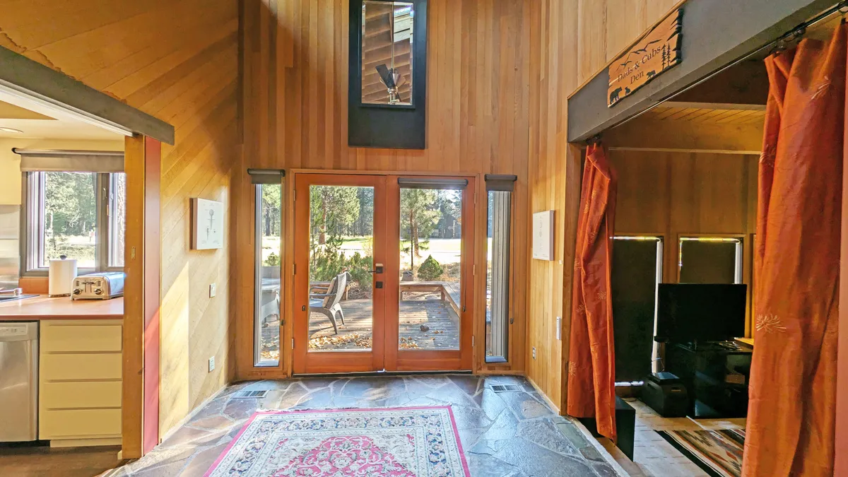 This image showcases double glass doors opening onto the outdoors, framed by warm wooden wall paneling and a cozy decorative rug, creating a seamless transition between interior comfort and the outside environment. The inviting seating area suggests a space ideal for relaxing while enjoying nature views or social gatherings.