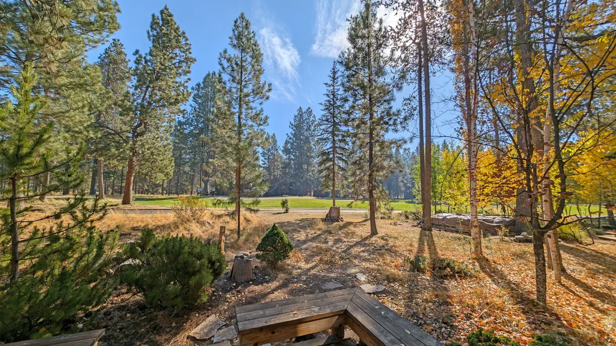 A scenic view across the golf course framed by tall trees and colorful foliage, with a comfortable wooden seating area nearby. The image captures the serenity and beauty of the outdoor setting, ideal for watching golfers or soaking in the natural surroundings.