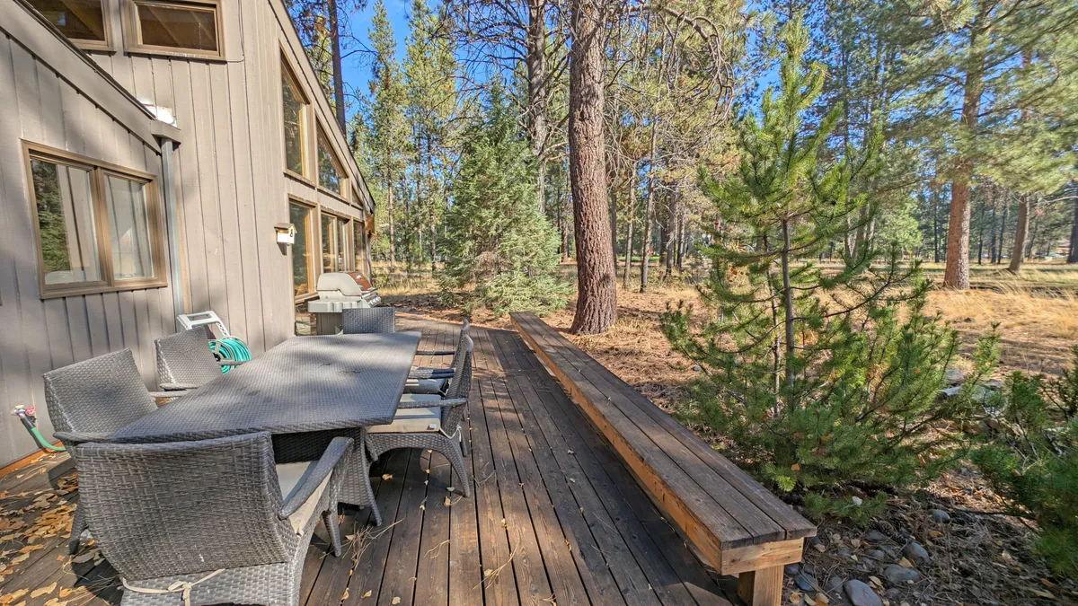 An inviting exterior view of a wooden deck outfitted with an outdoor dining set, all framed by dense, mature trees. The setting encourages group gatherings, al fresco meals, and enjoying the peaceful woodland backdrop, mirroring the post-game socializing and grilling described in the narrative.