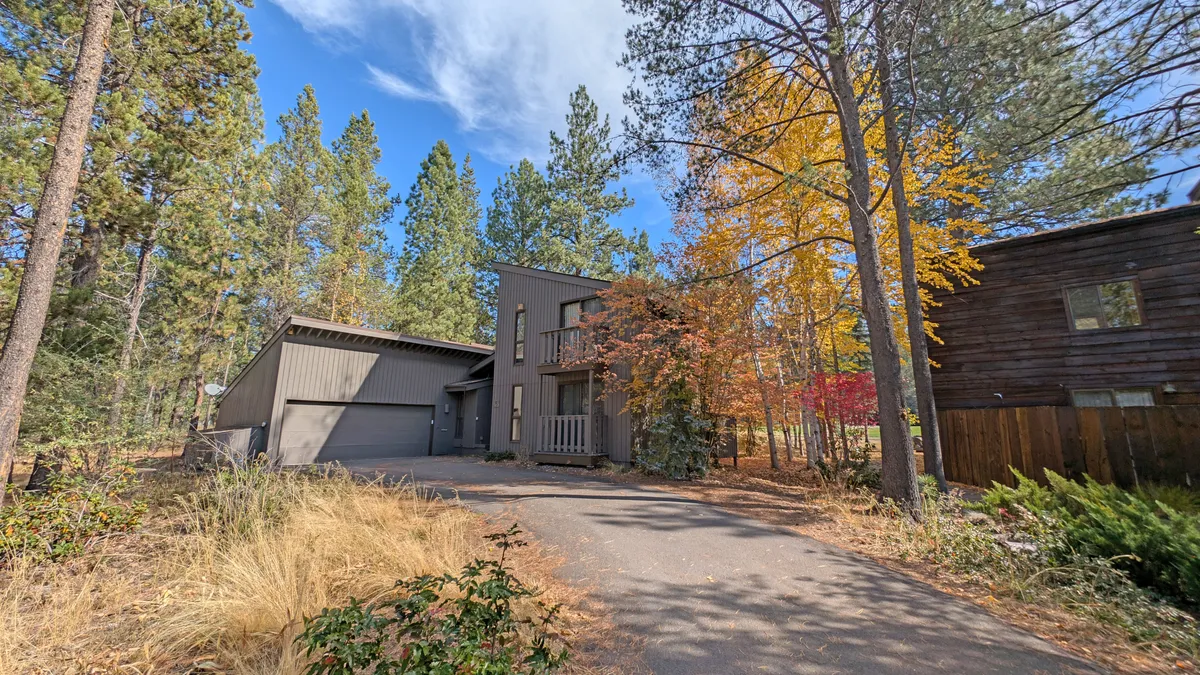 An exterior view of the home highlights modern architecture, colorful autumn foliage, and a spacious driveway leading to the house. This perspective hints at easy access for gear, bikes, and the potential location of an EV charging station.