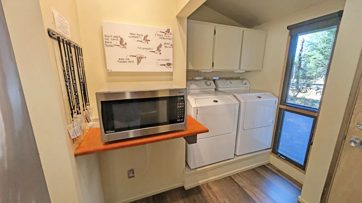 A mudroom or utility space is shown, featuring a microwave, washing machines, wooden countertop, and wall art. The area looks functional and welcoming—ideal for pre- and post-adventure clean-up, pet care, or snack preparation.