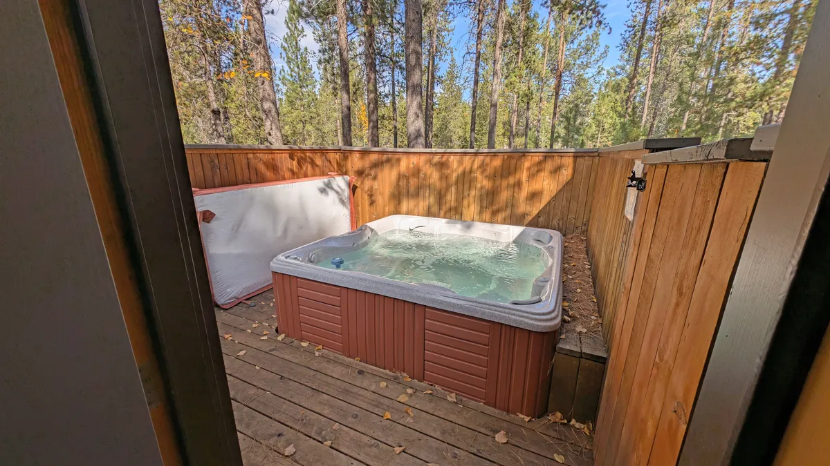 A tranquil outdoor scene with a hot tub on a wooden deck immersed in nature. The setting is ideal for unwinding after a day’s activities, with the option to stargaze or simply enjoy the peaceful ambiance.
