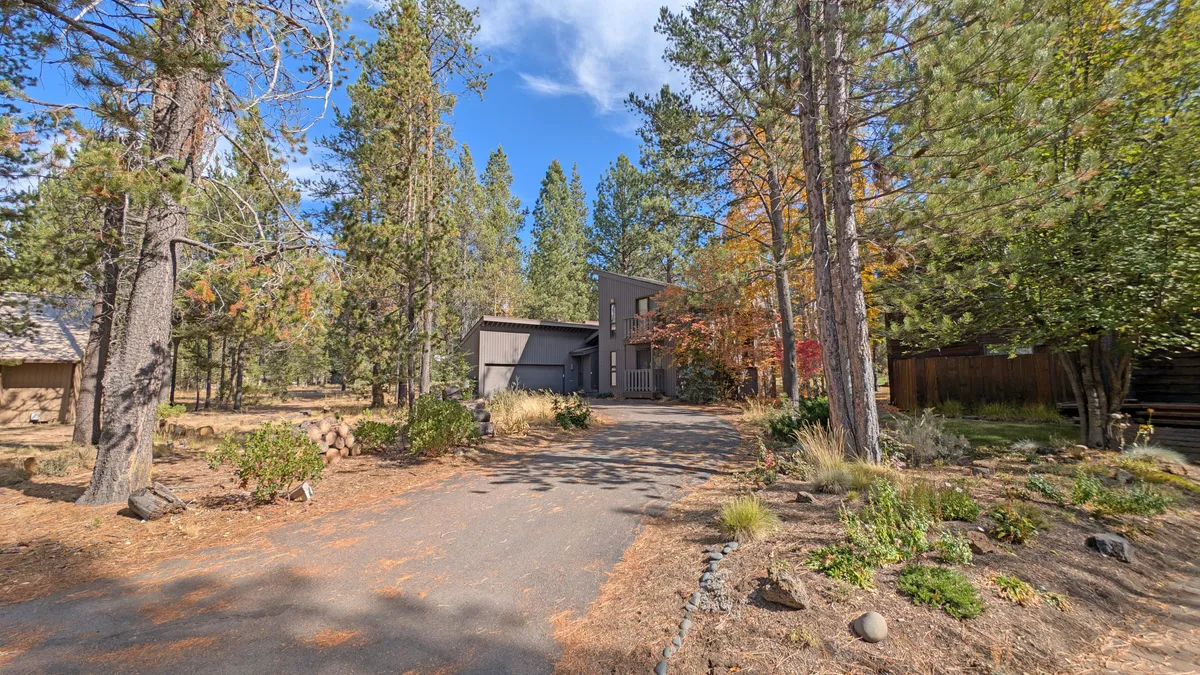 A modern house nestled amidst mature trees, with a driveway leading up to the entrance. The tranquil surroundings evoke a sense of adventure just outside the door, with plenty of space for gathering and staging outdoor excursions.